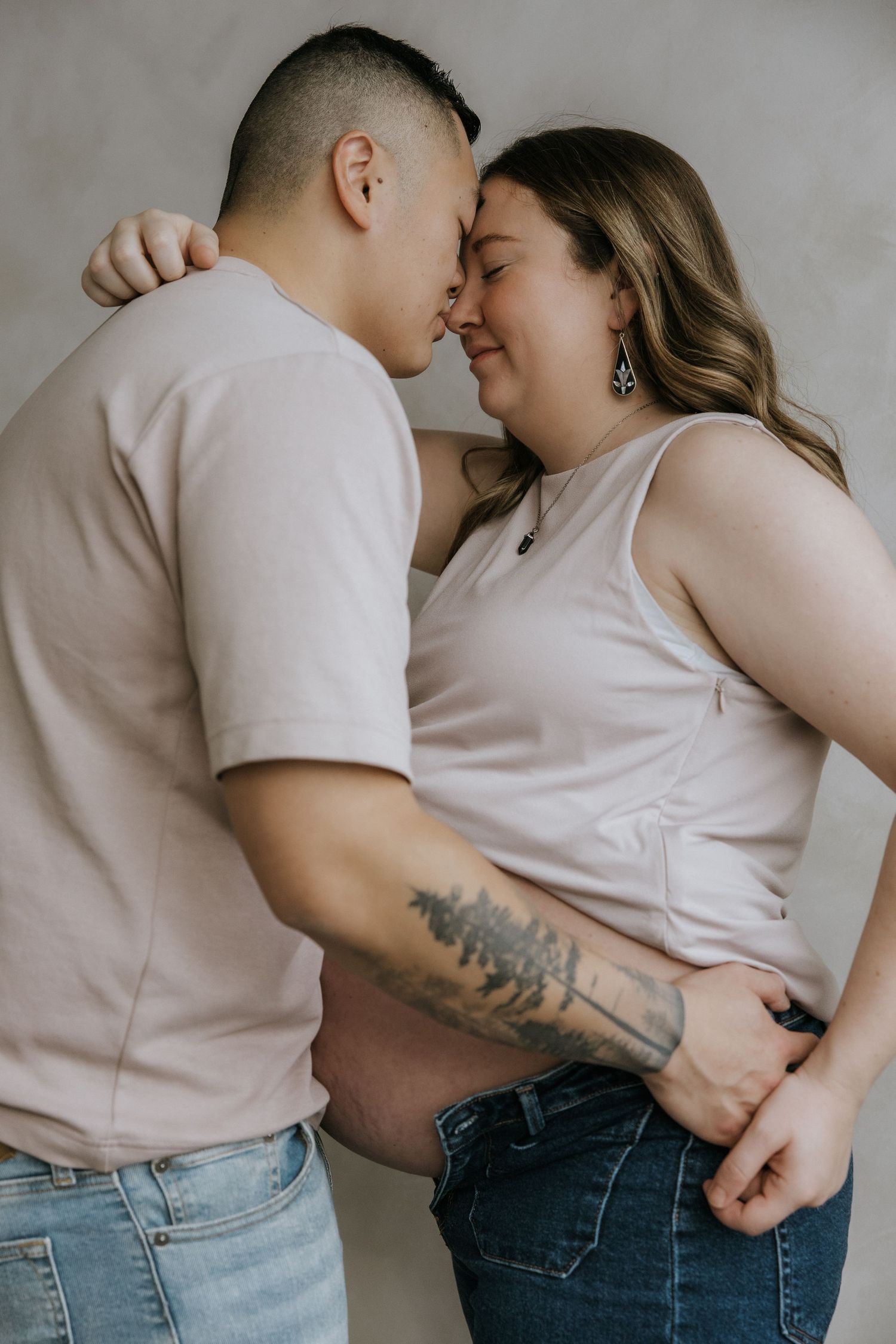 A tender maternity photo sequence showing a couple embracing in soft, neutral tones against a light background.