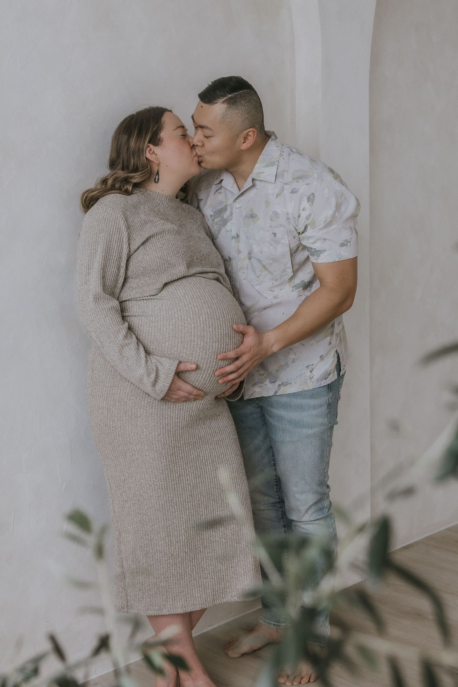 A couple shares an intimate moment in a light-filled room with minimal decor and soft neutral tones.