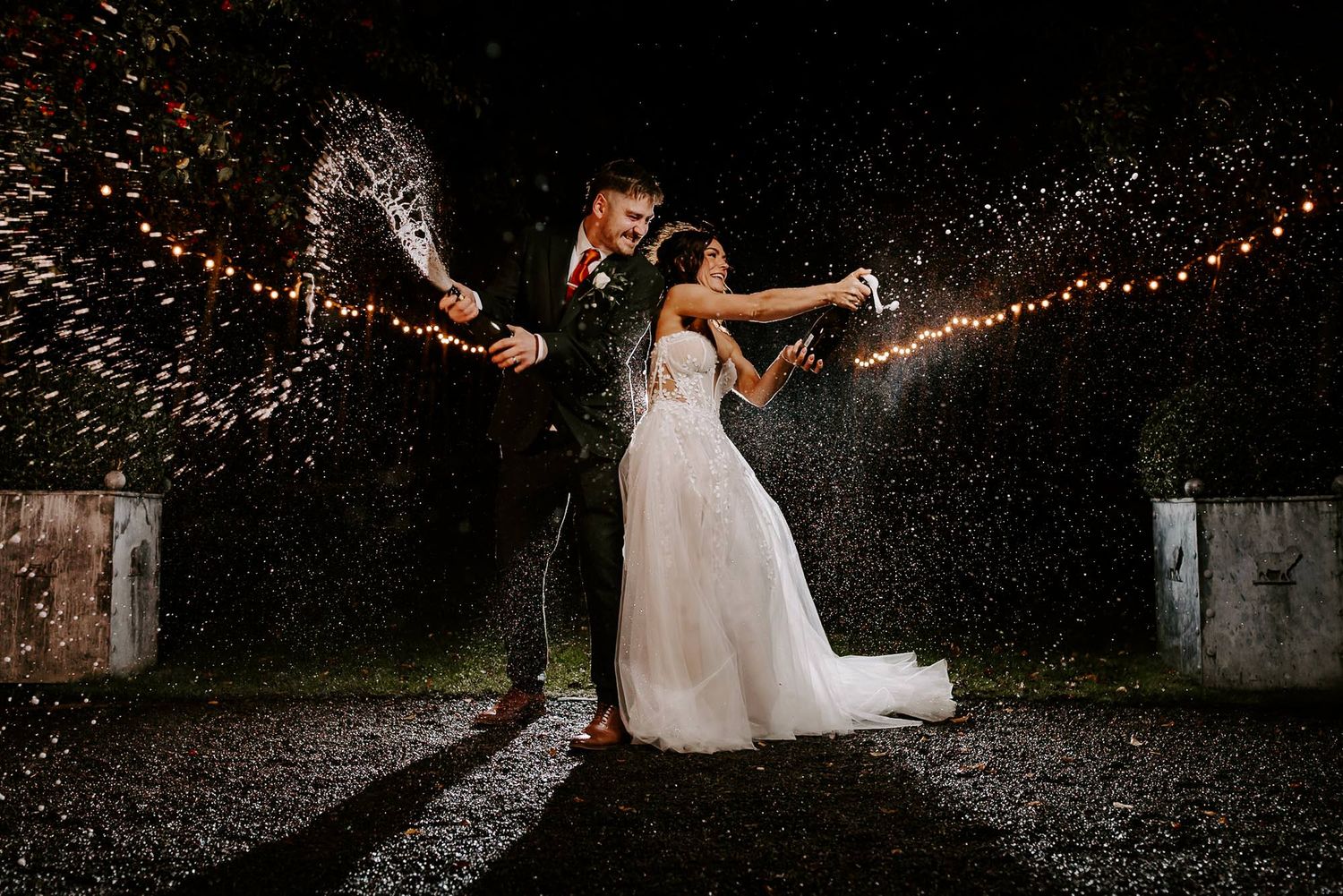Couple creates magical sparkler display at night under string lights during outdoor wedding celebration.