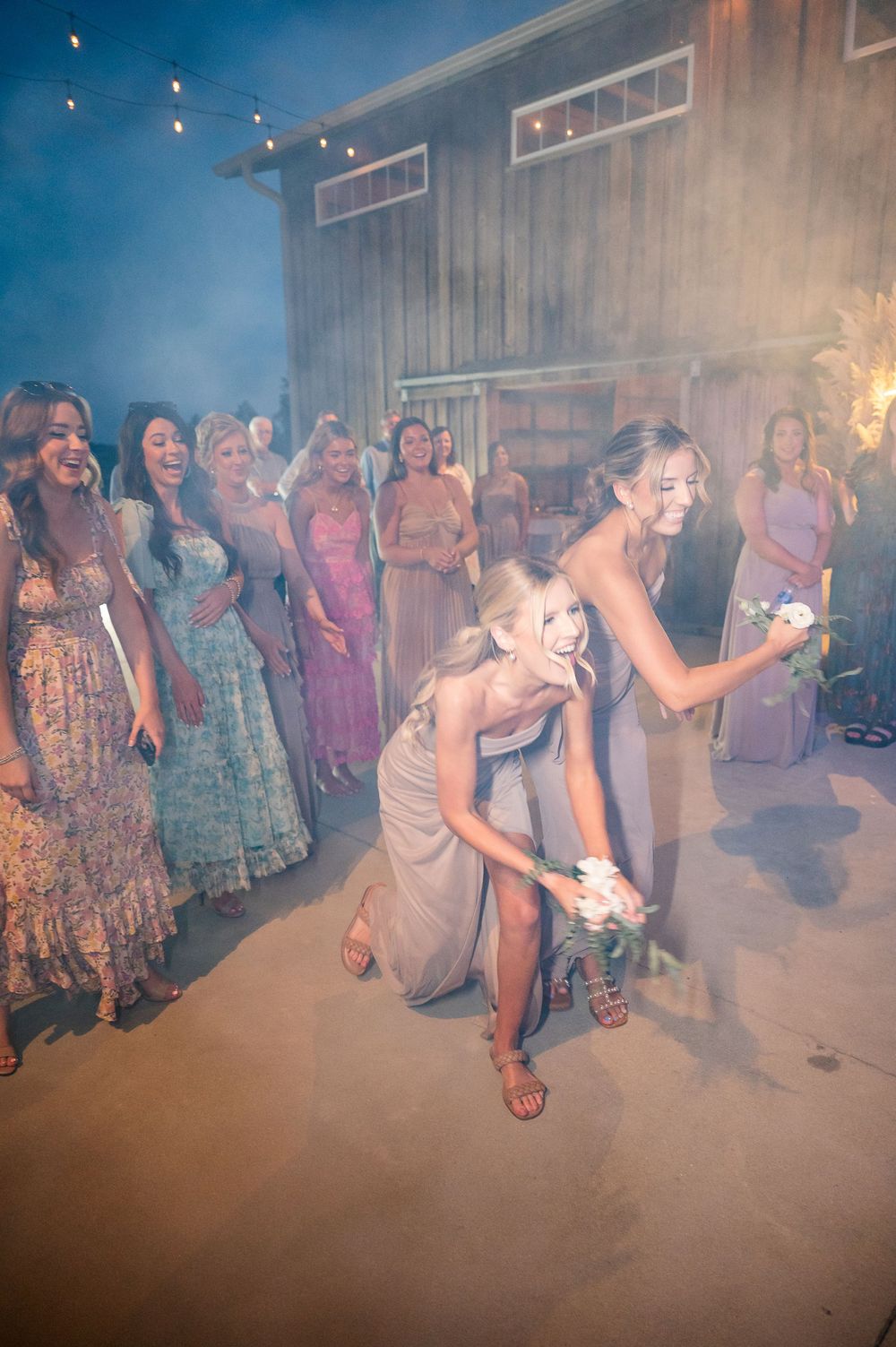 Wedding guests dance through atmospheric smoke effects at an outdoor evening reception.