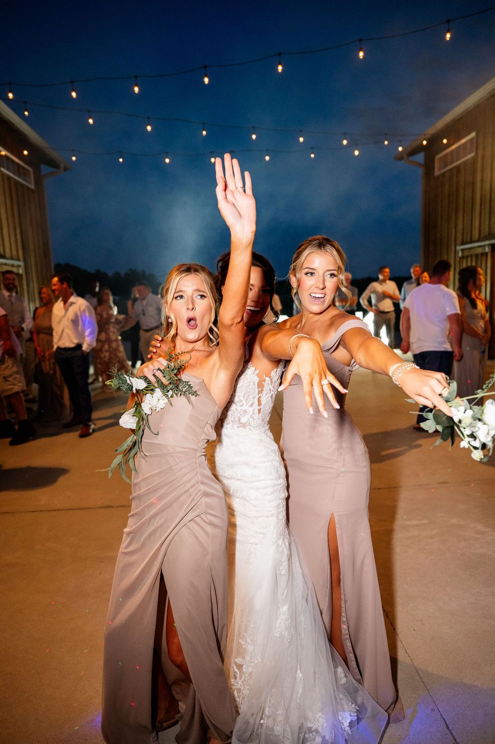 Wedding guests dancing and celebrating at an outdoor reception with string lights overhead.
