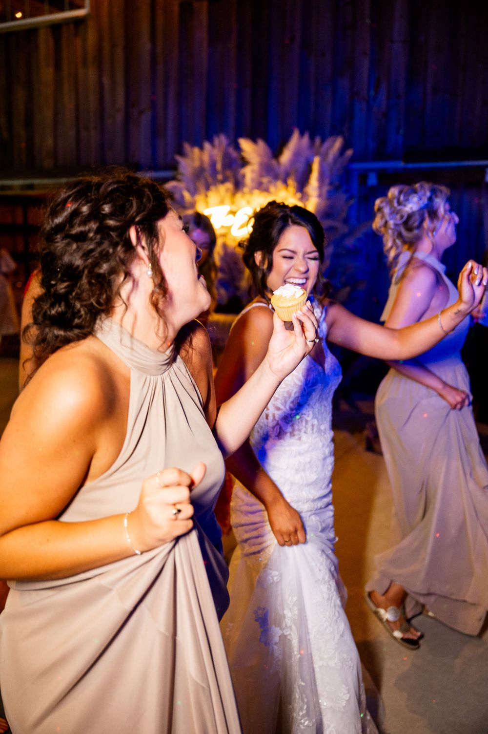 Bridesmaids in taupe dresses dancing enthusiastically at a wedding reception.