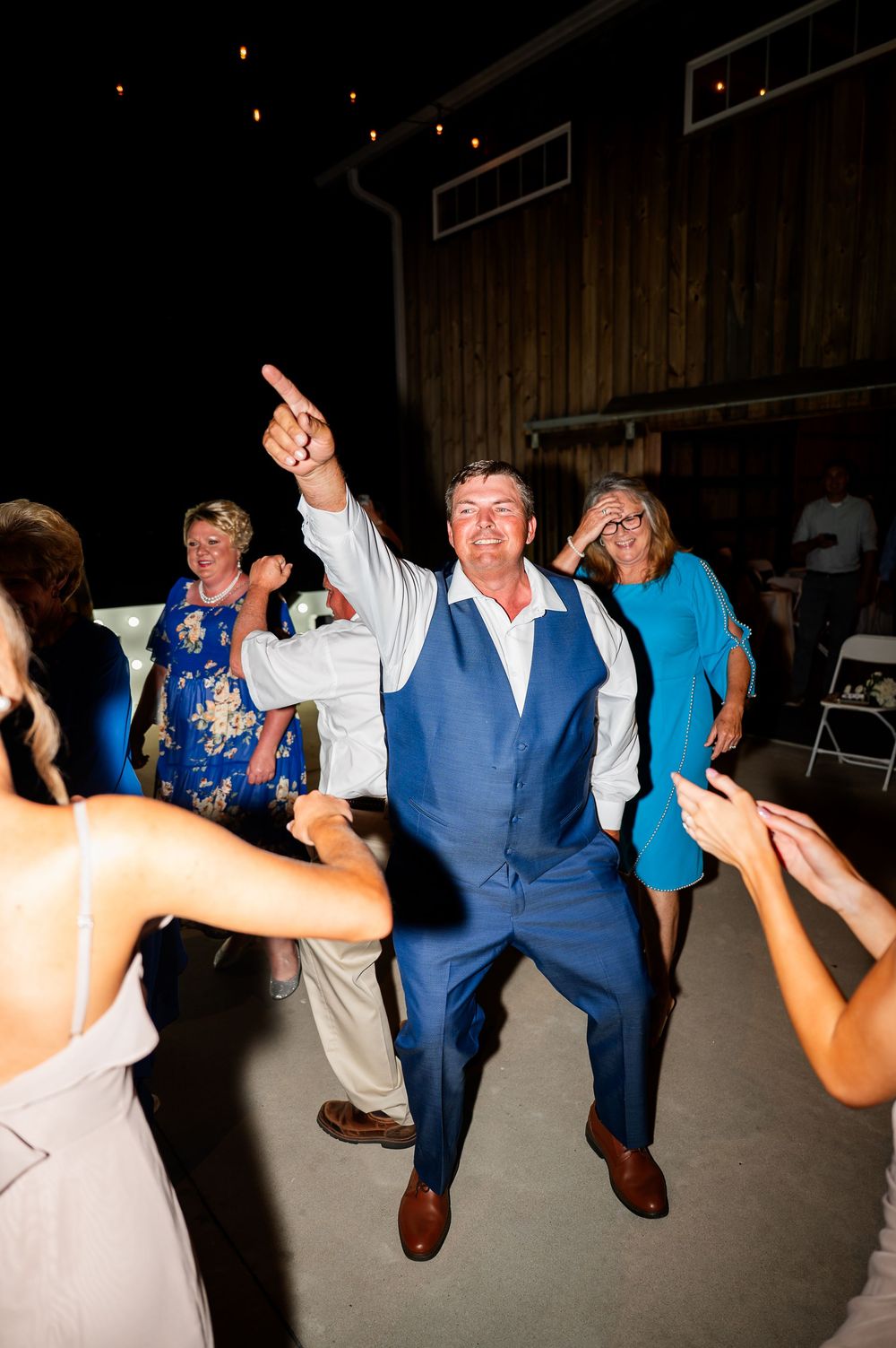 Wedding party members jumping and dancing in formal attire at an indoor reception.