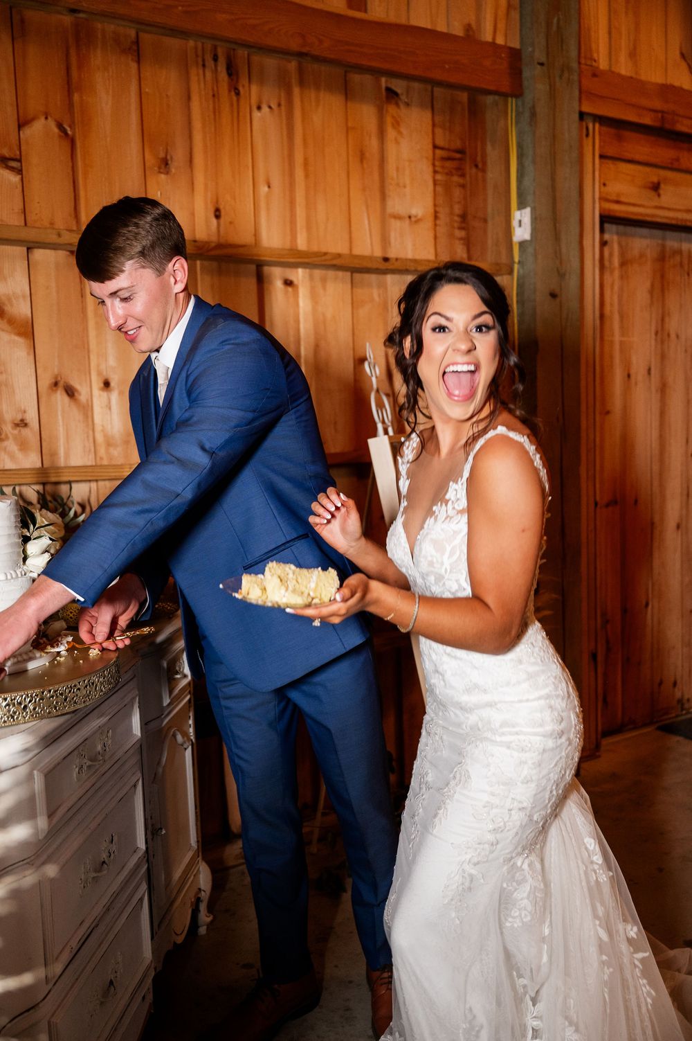 A playful cake-cutting sequence in a rustic wooden barn setting at a wedding reception.