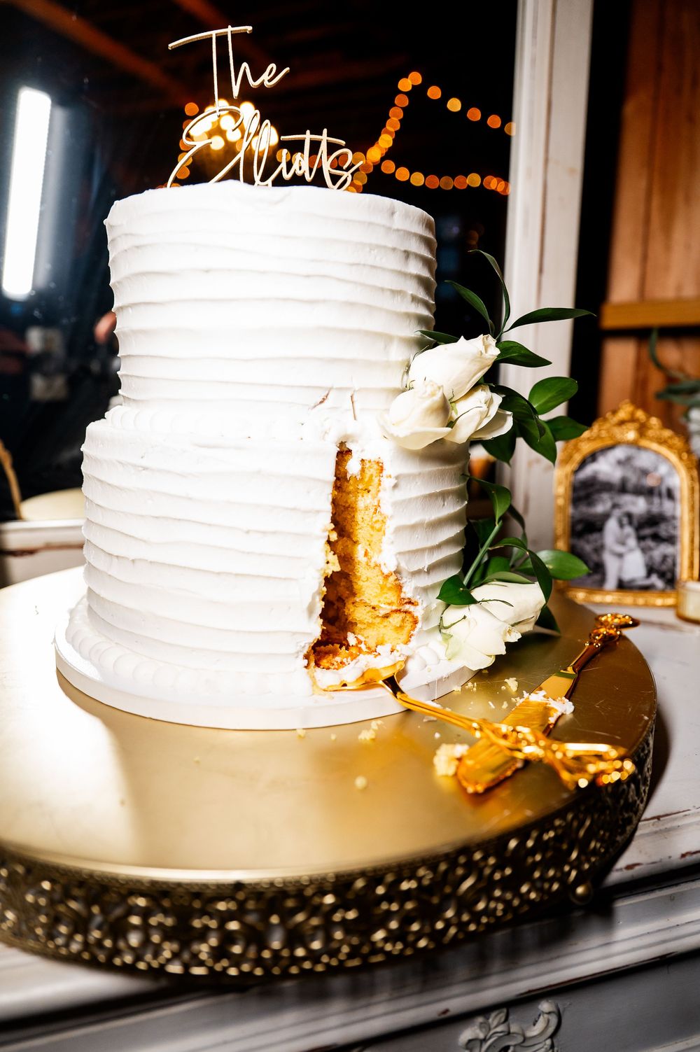 An elegant white wedding cake with textured frosting and gold accents displayed on a decorative stand.