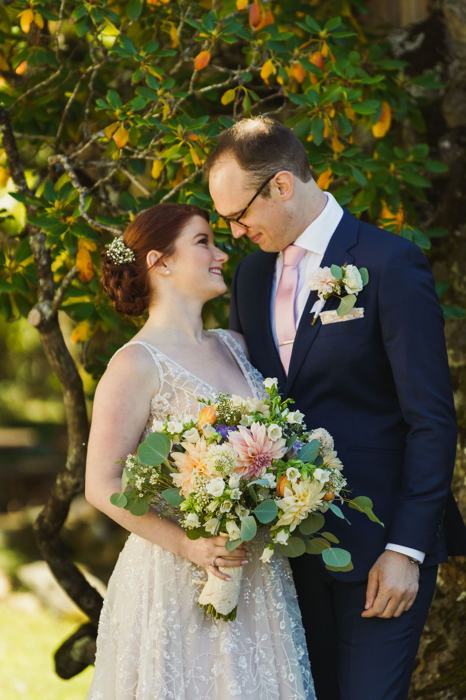 A couple shares a romantic moment with a colorful bouquet against orange blossoms.