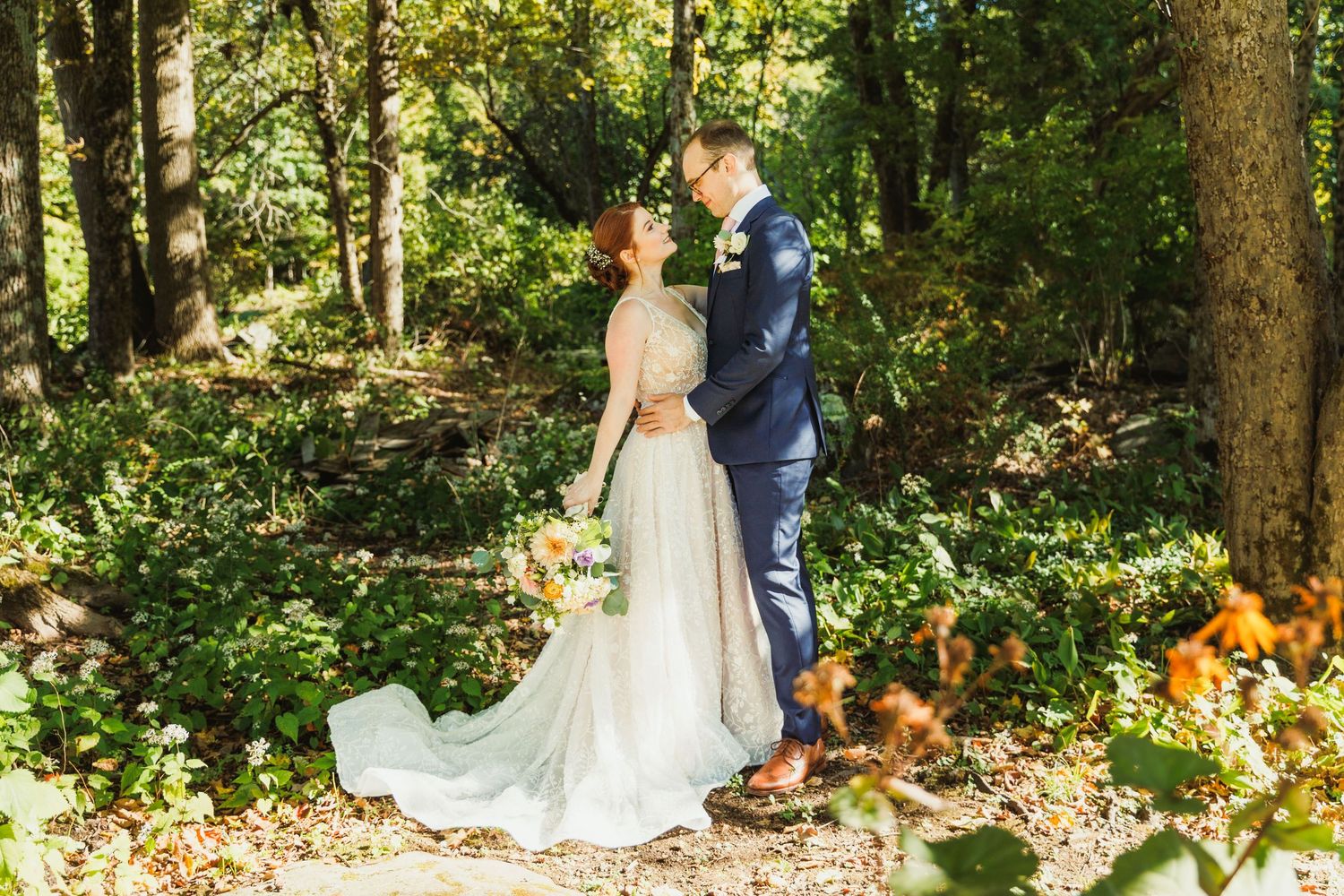 A couple poses together in a sunlit forest setting during their wedding photoshoot.