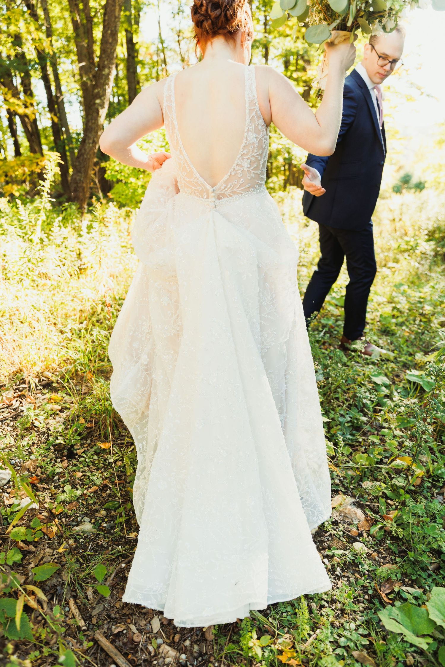 Wedding couple walks through a lush forest setting with golden sunlight filtering through trees.