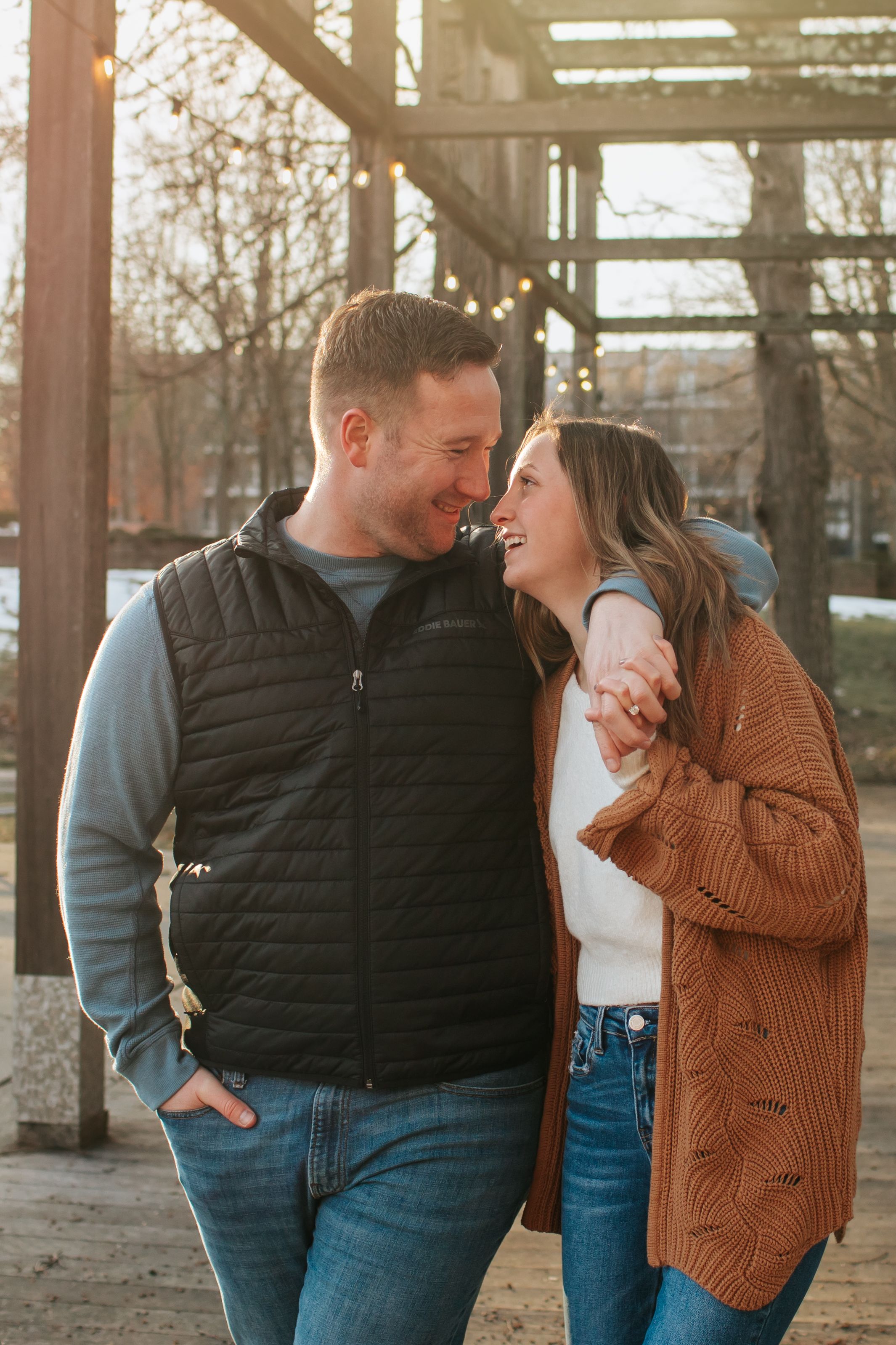 Couple shares intimate moments under wooden pergola at sunset.