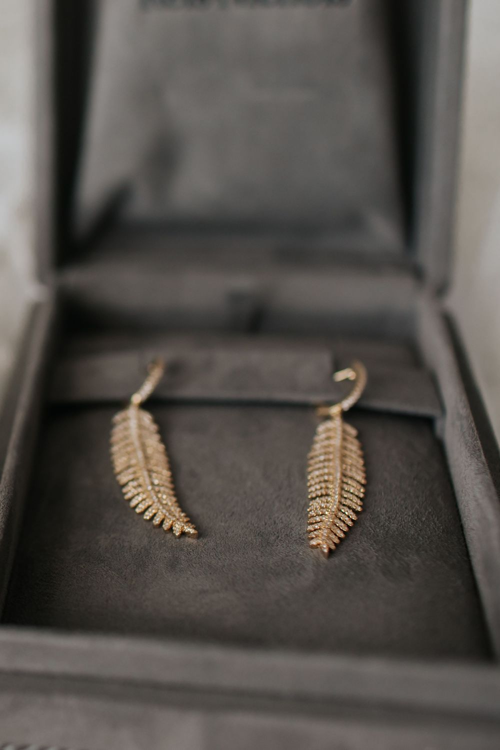 Delicate gold leaf or fern-shaped earrings displayed in a series of black jewelry boxes.