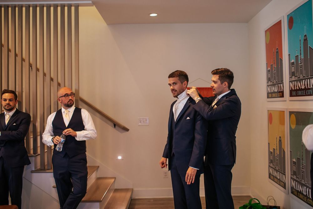Groomsmen in navy suits gather in a modern indoor venue with wooden accents and recessed lighting.