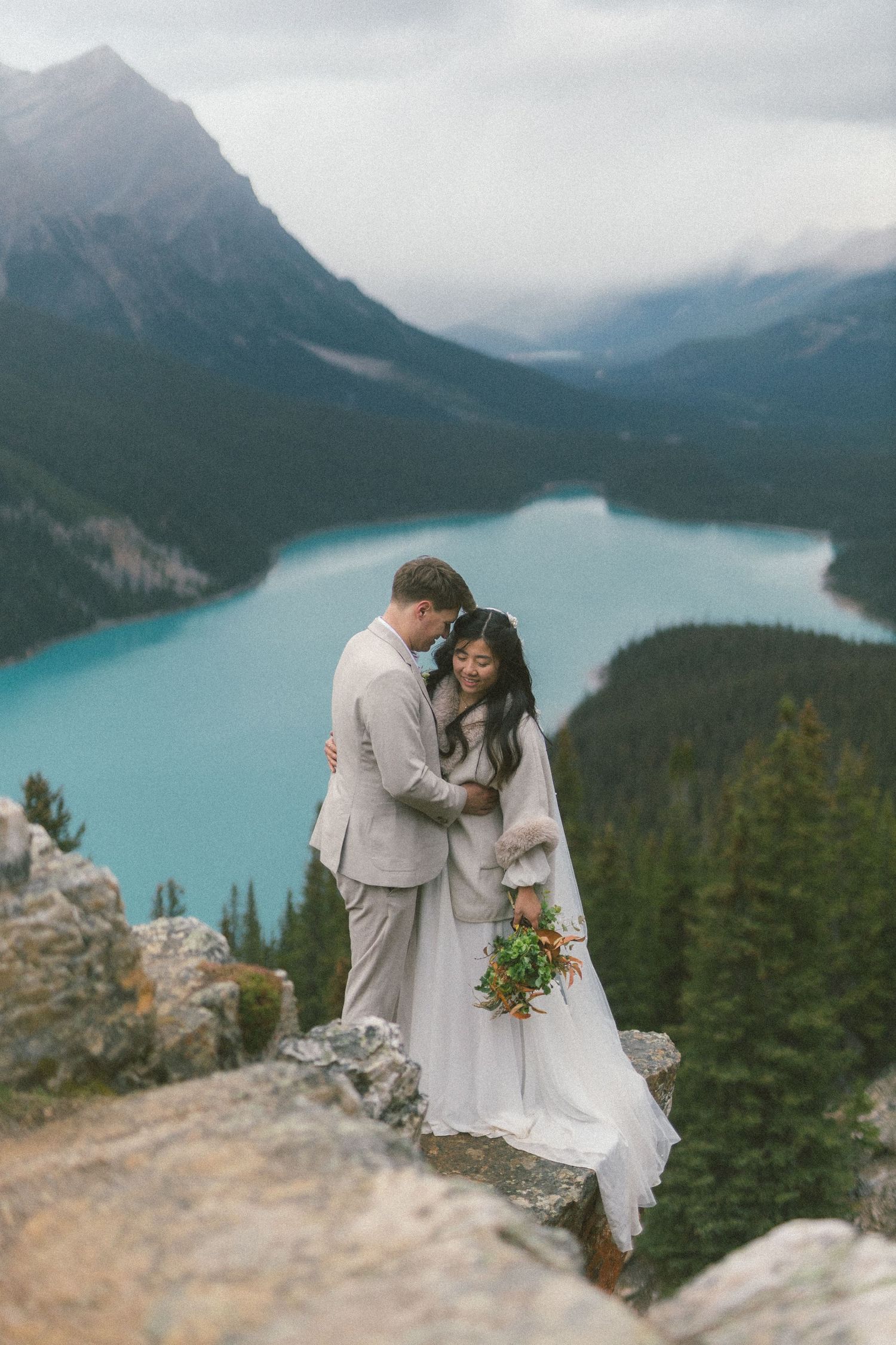 bride and groom cuddle and laugh on a rocky outcrop above Peyto Lake in Banff