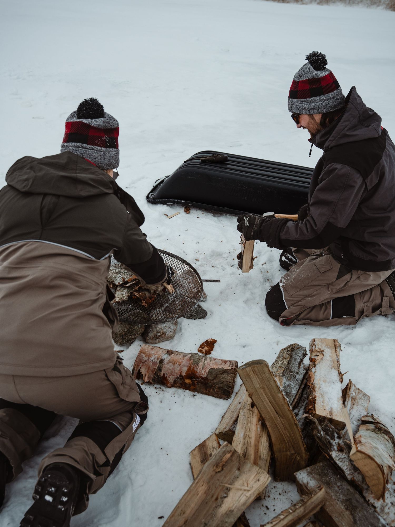Person setting up ice fishing equipment while kneeling in snowy conditions.