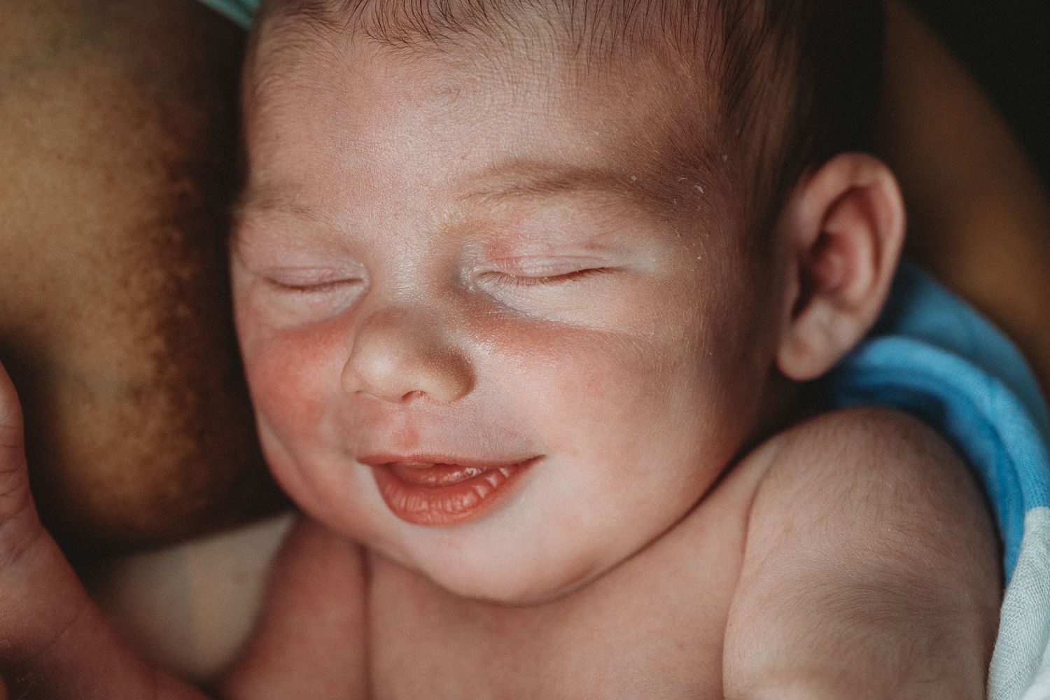 Close up of a sleeping newborn baby with rosy cheeks and peaceful smile.