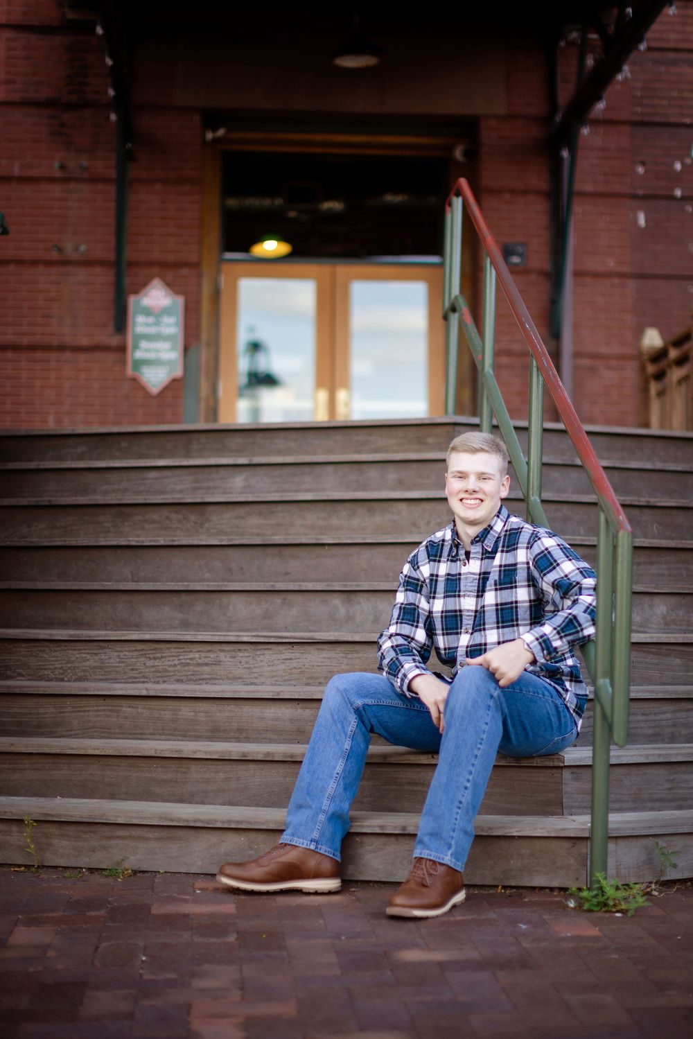 A series of three connected photos showing someone sitting on wooden steps outside a brick building wearing jeans and plaid.