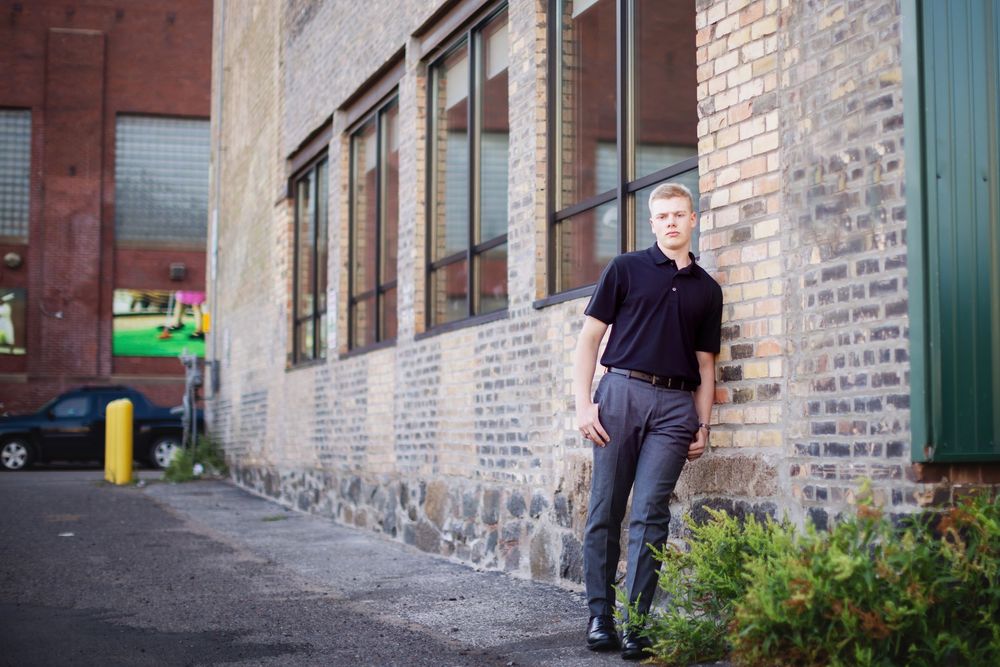 Person walking past brick wall with green doors in an urban alley setting.