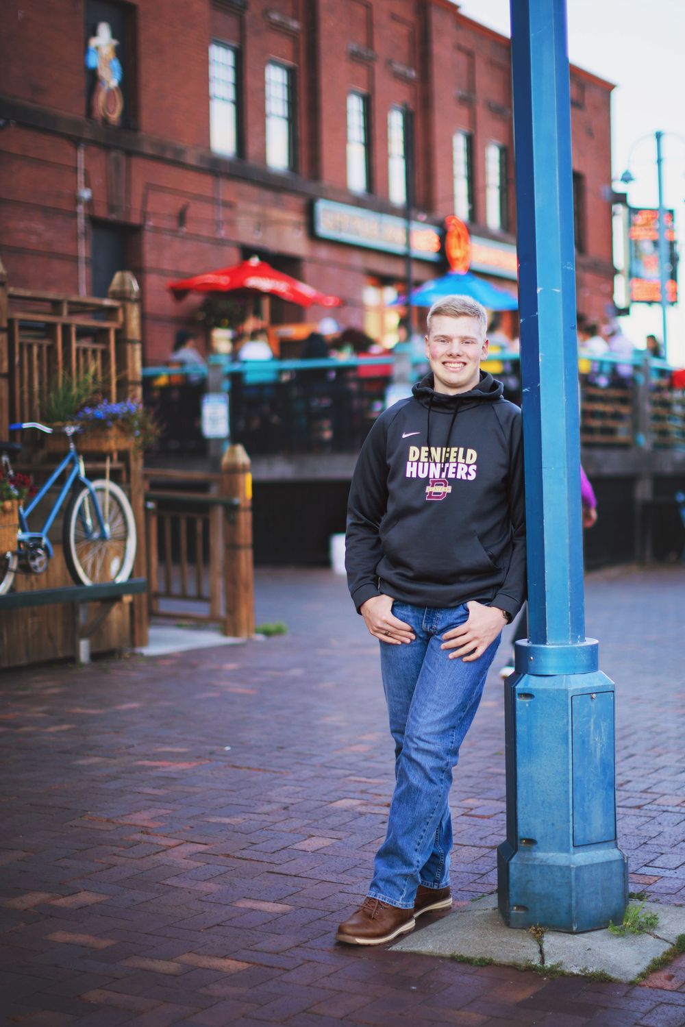 Three connected photos showing a person in casual wear leaning against a blue pole on a brick sidewalk.