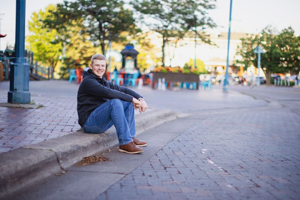Person wearing blue jeans and brown shoes sits on brick steps in an urban setting during daytime.