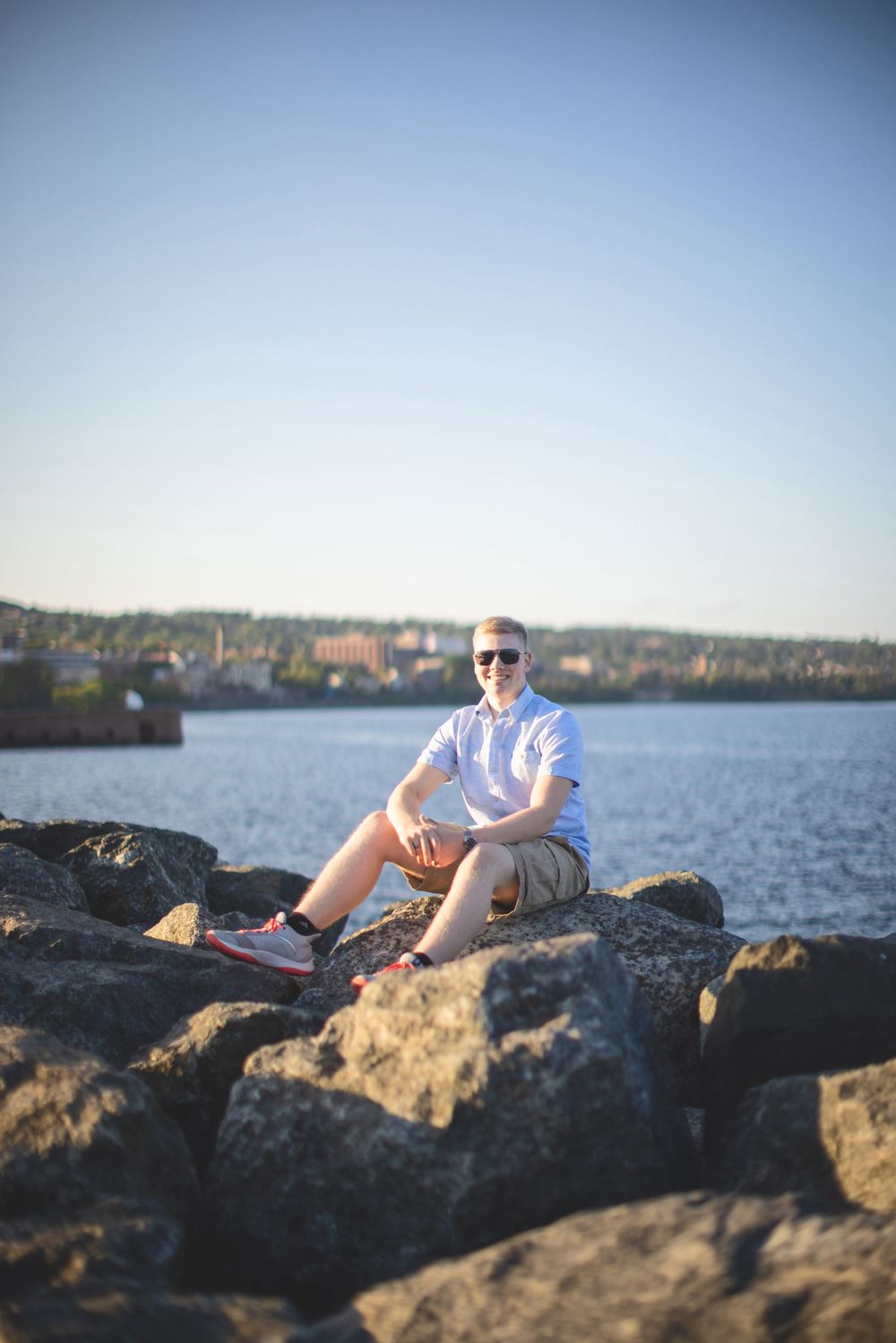 A person in white relaxes on rocky coastal outcroppings near a waterfront at sunset.