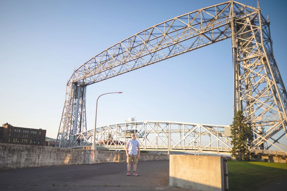 Person stands beneath the iconic Aerial Lift Bridge at sunset in Duluth, Minnesota's Canal Park district.