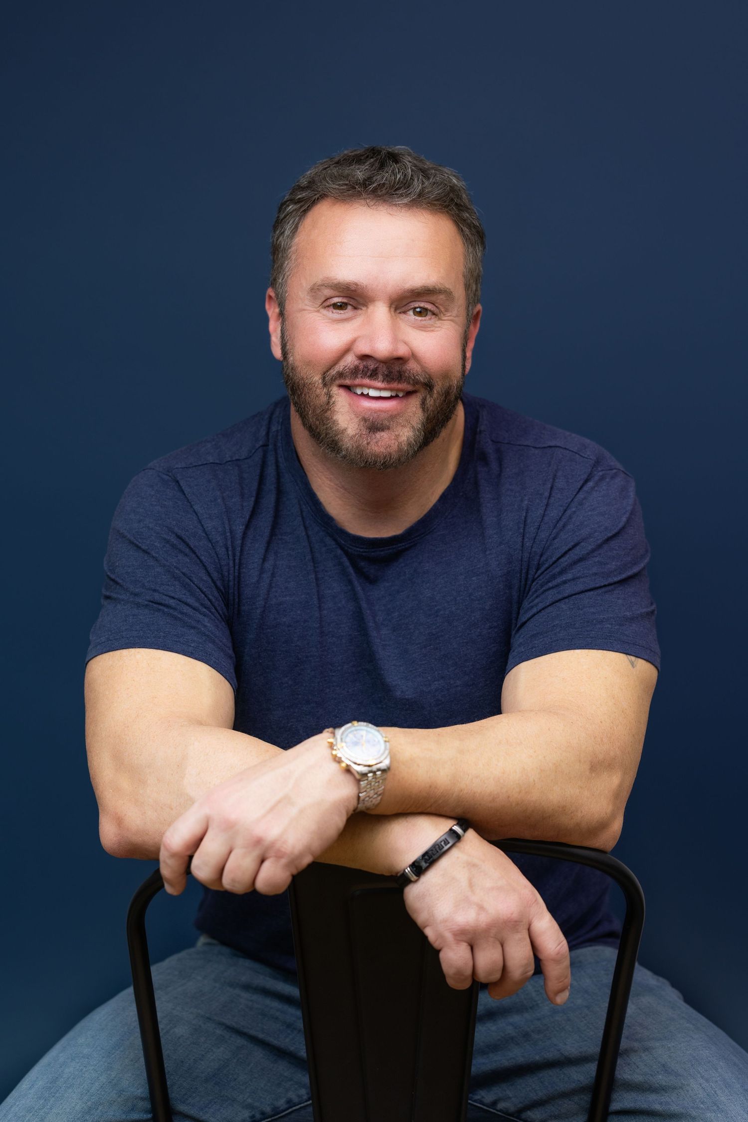 A person in a sleeveless white top and black pants poses against a light background with a bright smile.