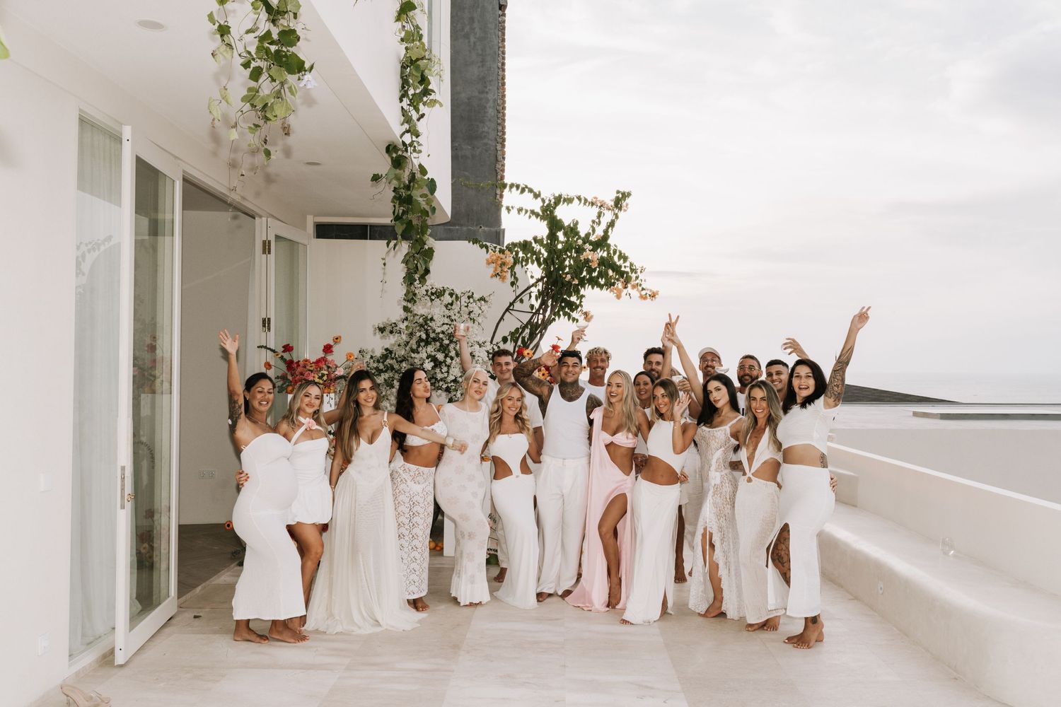 A group of people dressed in white outfits pose together in a modern, light-filled space.