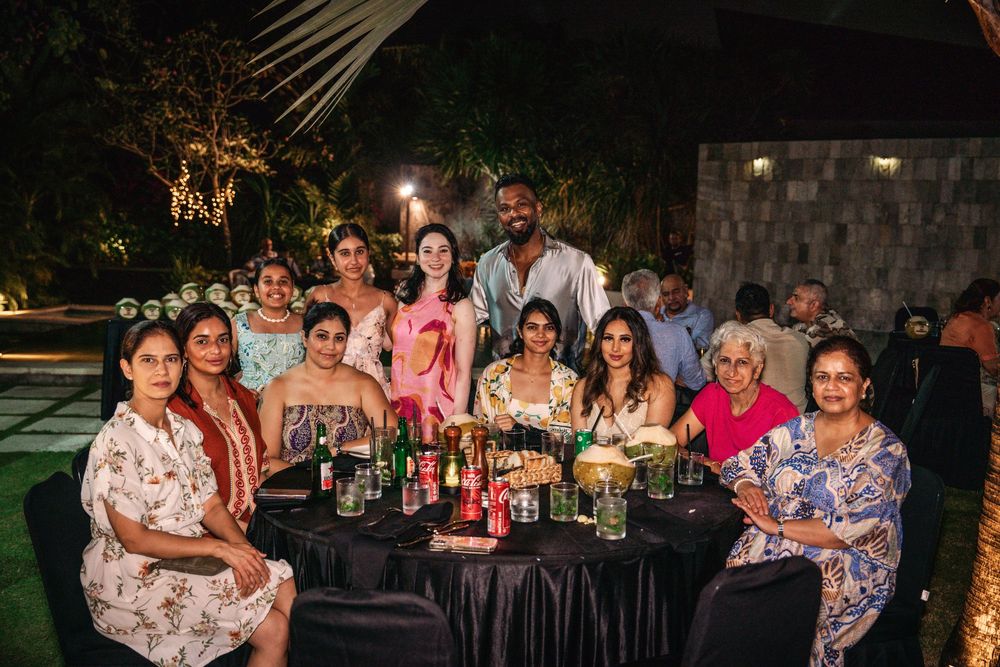 A group of people sit at a long dining table outdoors at night during a festive gathering.