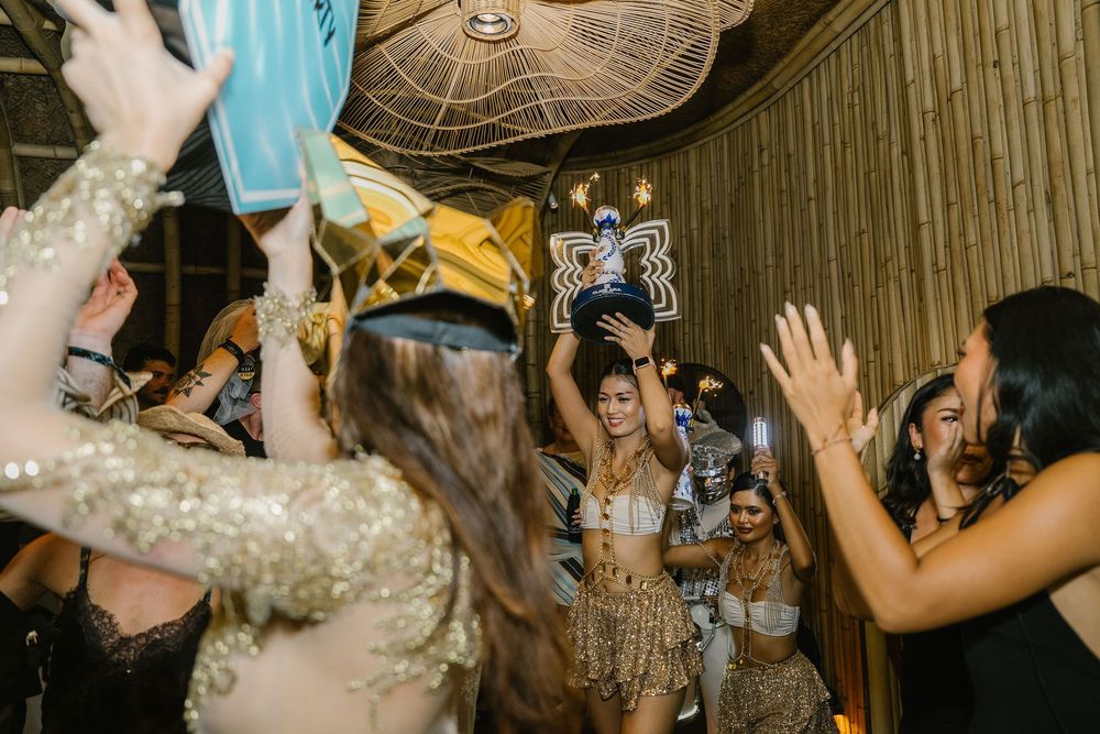 Women celebrating at a party, dancing and raising balloons in a festive venue with warm lighting.