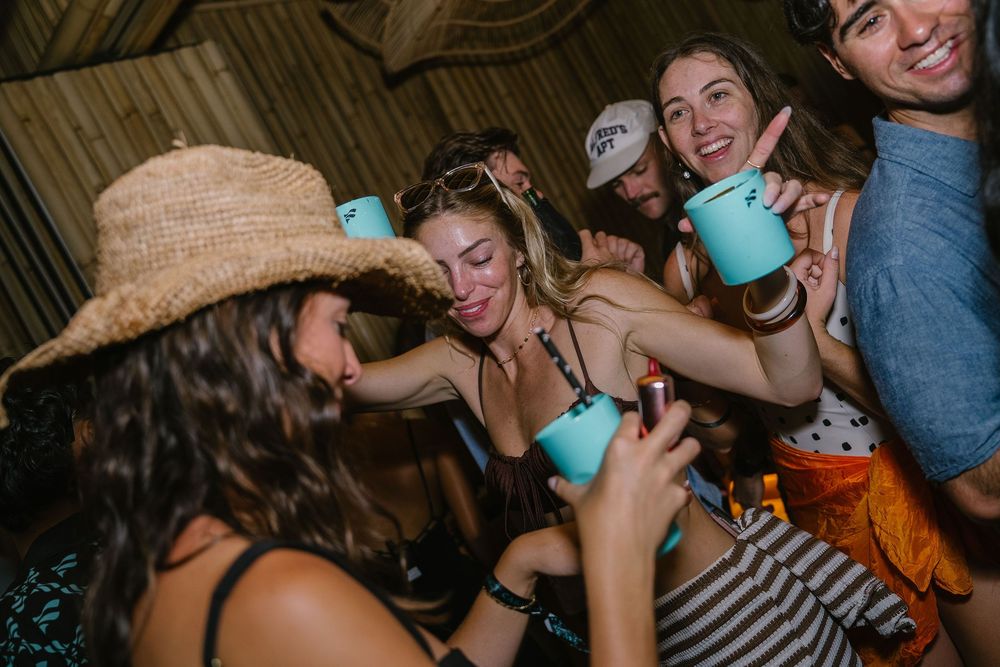 Group of young friends smiling and toasting with teal cups at an outdoor party event.