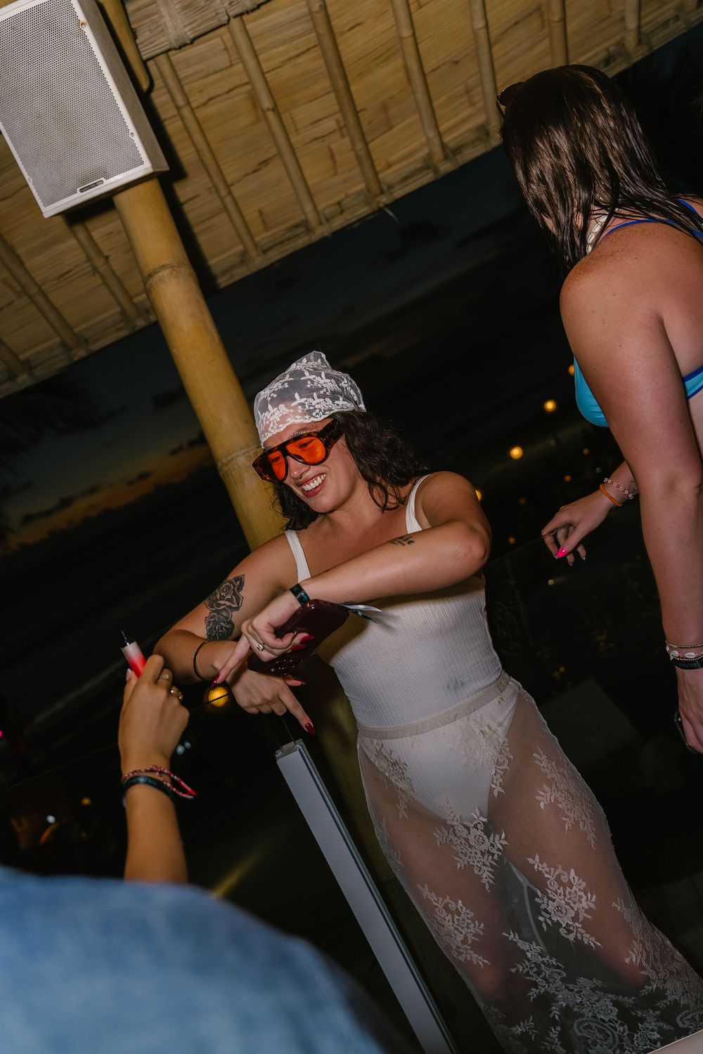 Woman in white lace outfit and red sunglasses smiling at a nightclub party event.