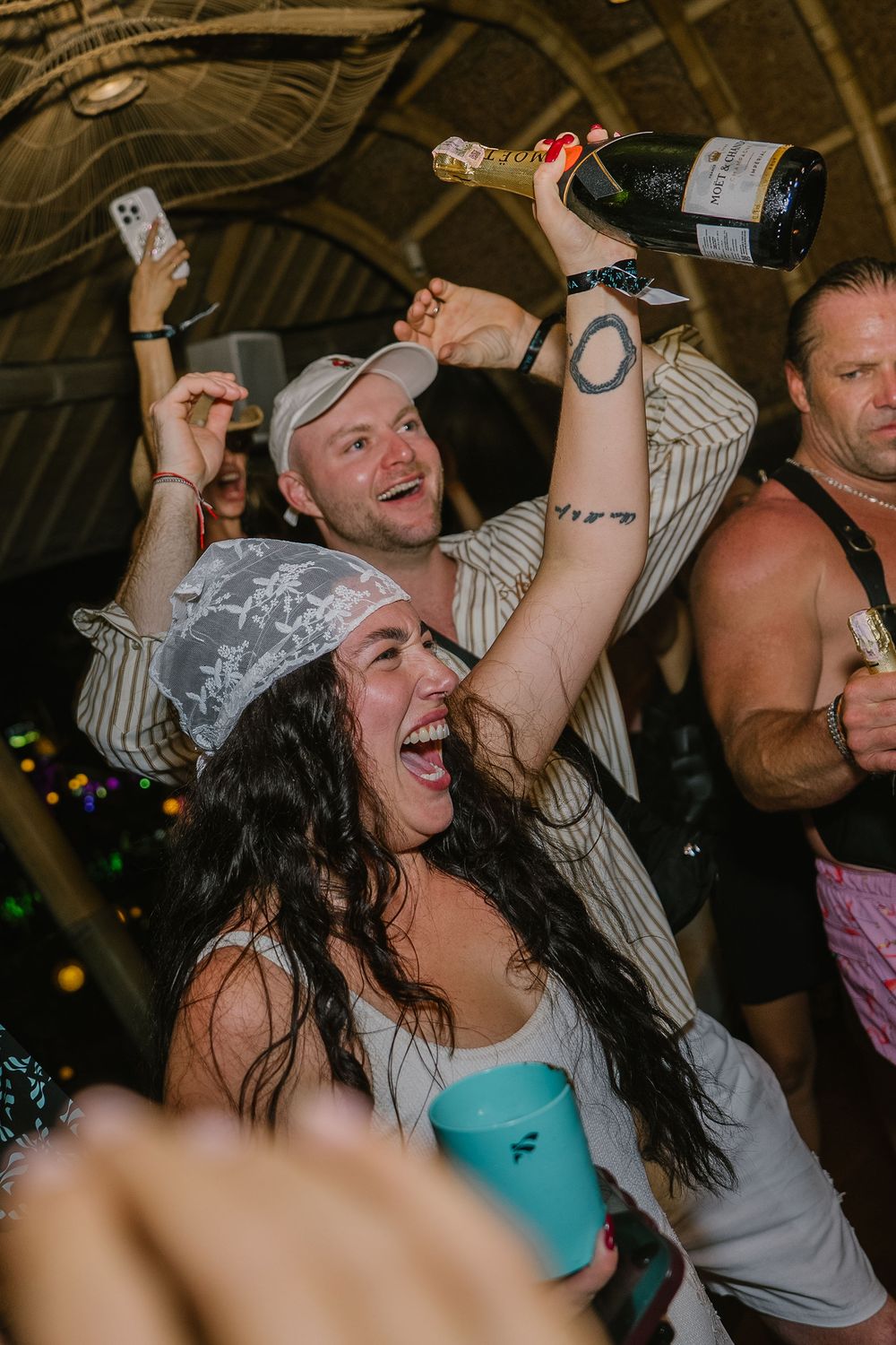 Excited party guests celebrate indoors, with a woman raising a champagne bottle joyfully.