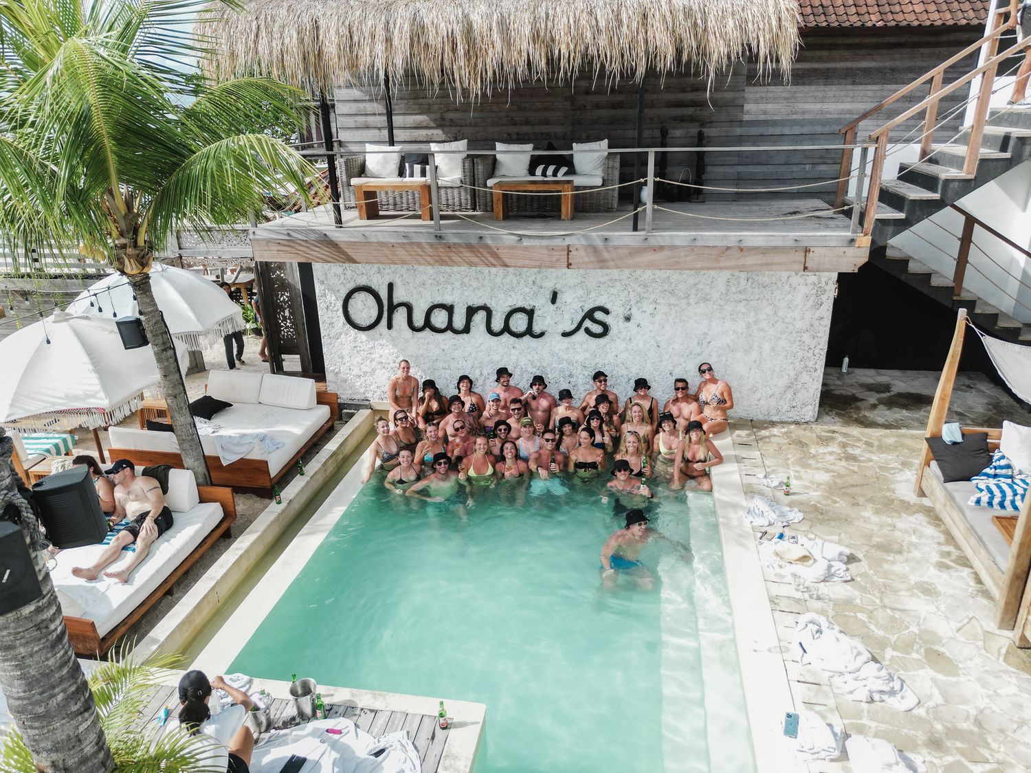 Aerial view of a swimming pool at Ohana's with a large group gathered in the turquoise water surrounded by palm trees.