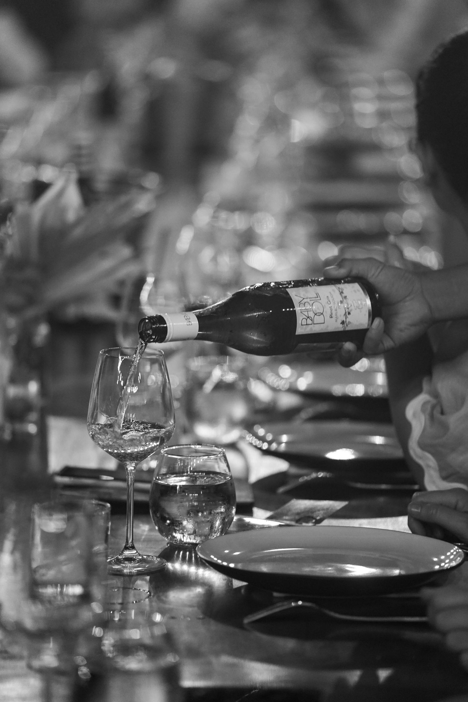 Black and white image of wine glasses and place settings on an elegant dining table in a dimly lit restaurant.