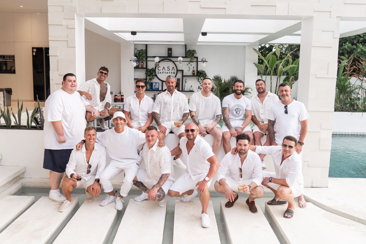 Group wearing white outfits sits together on white steps in coordinated casual attire.
