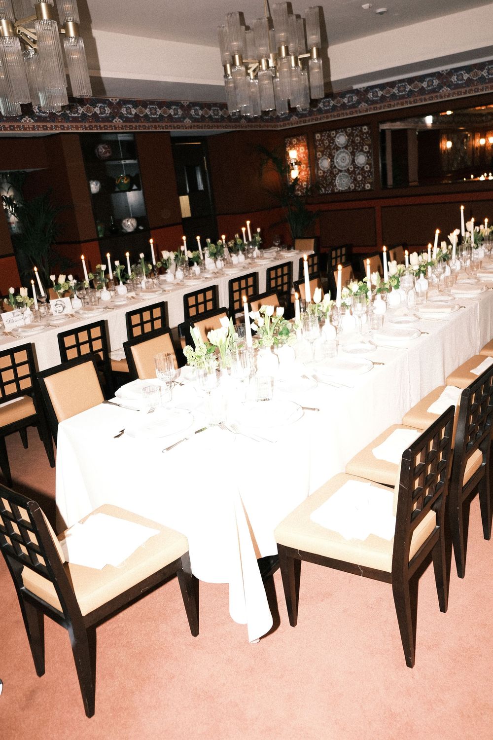 Long banquet tables set with white linens and elegant candle centerpieces in an upscale dining room.