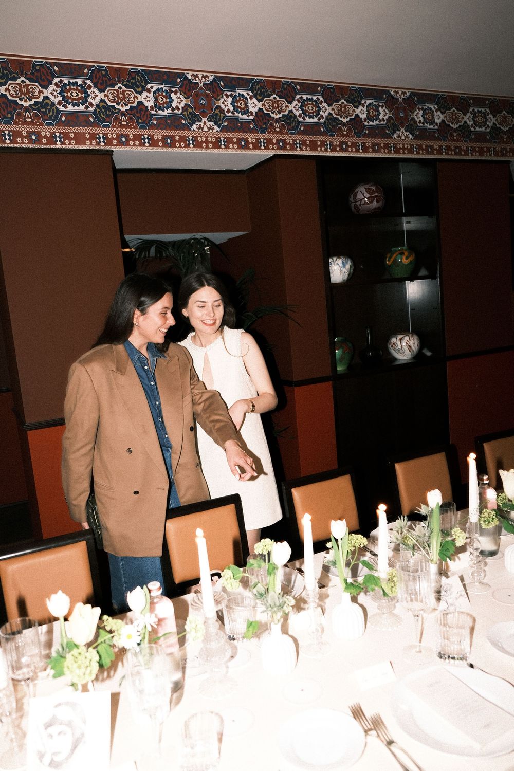 Formal dinner table setting with white candles and floral decorations along a brown-walled banquet room.