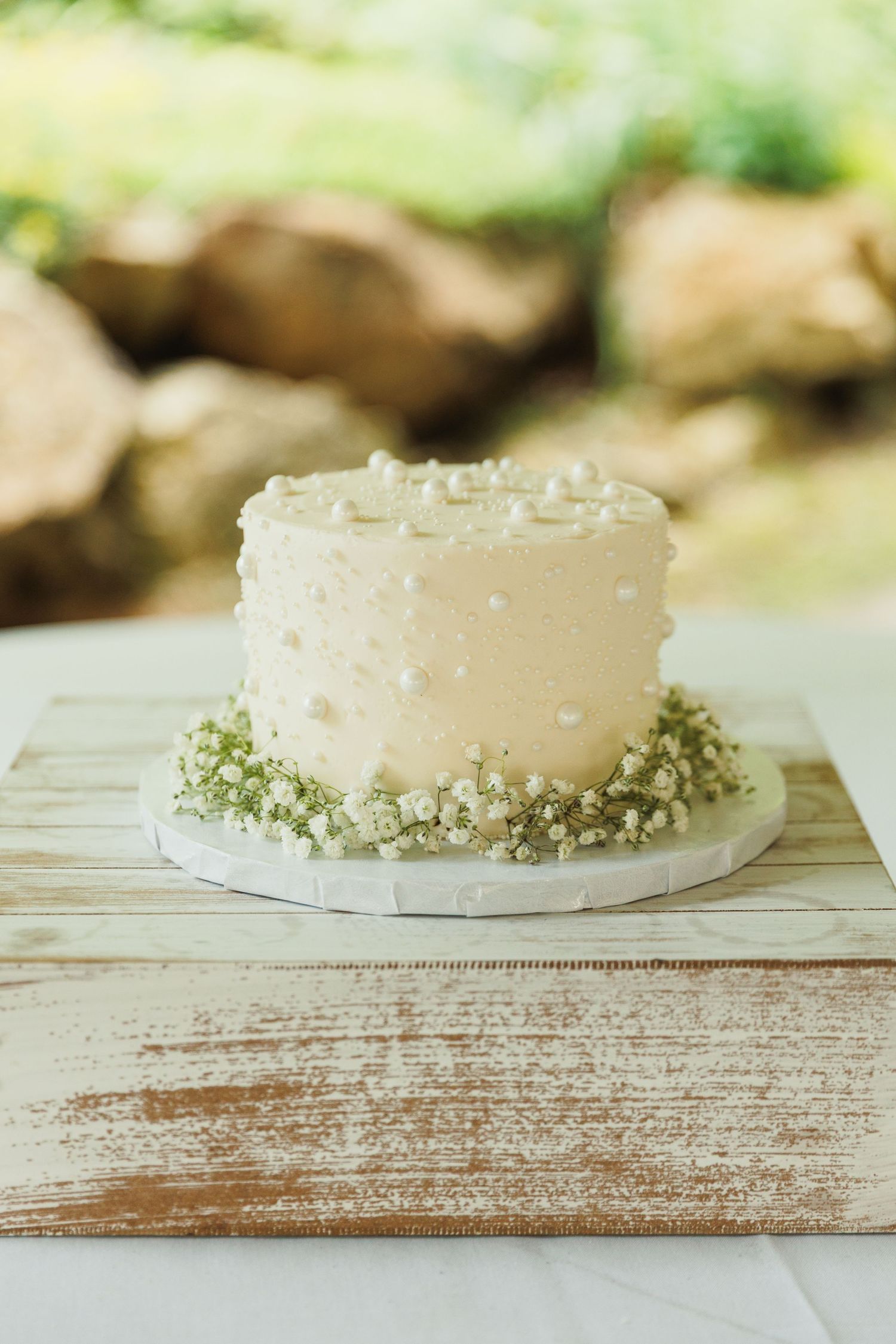 White frosted cake decorated with green garnish on rustic wooden surface.