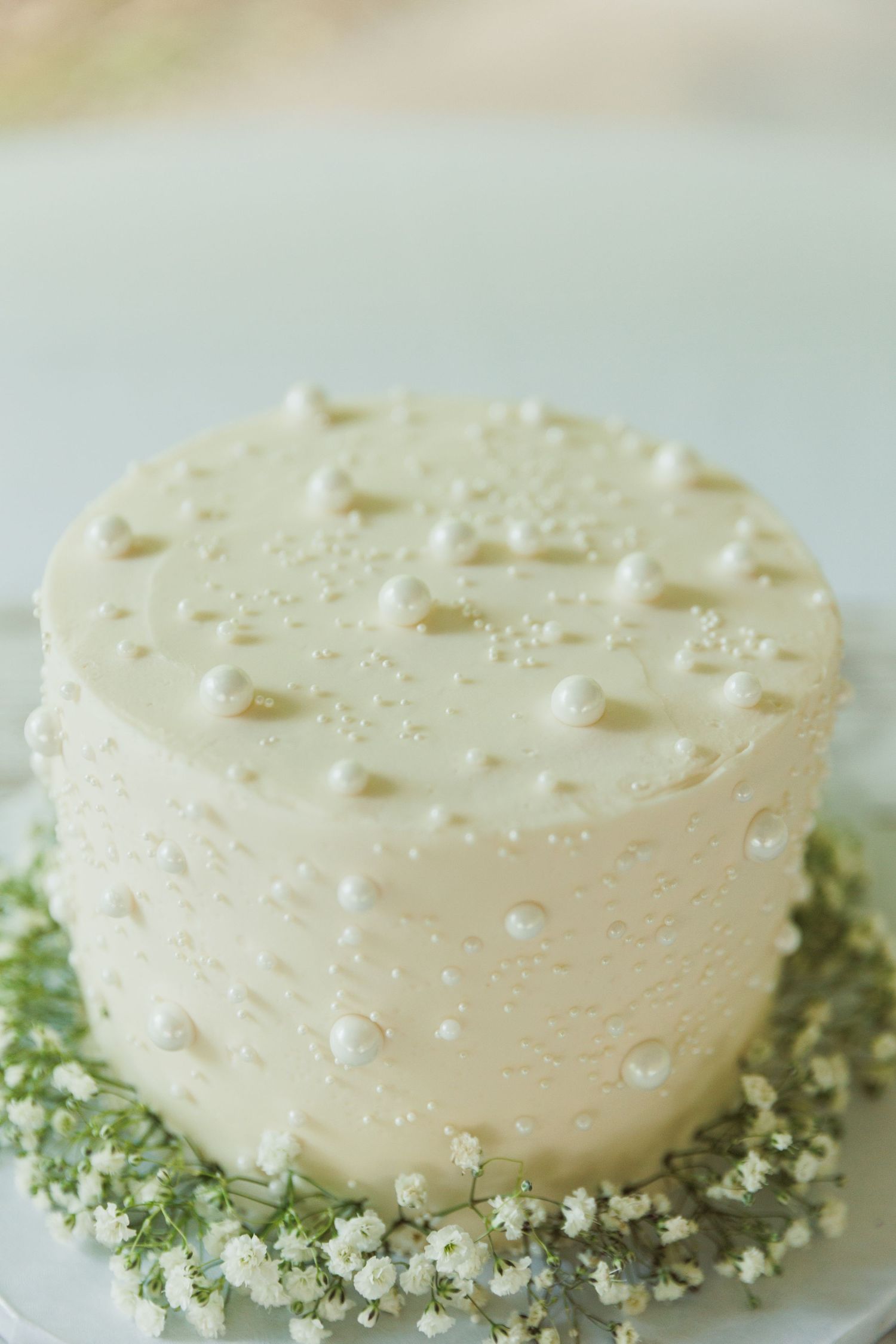 Close-up of white textured cake with pearl decorations and green garnish.