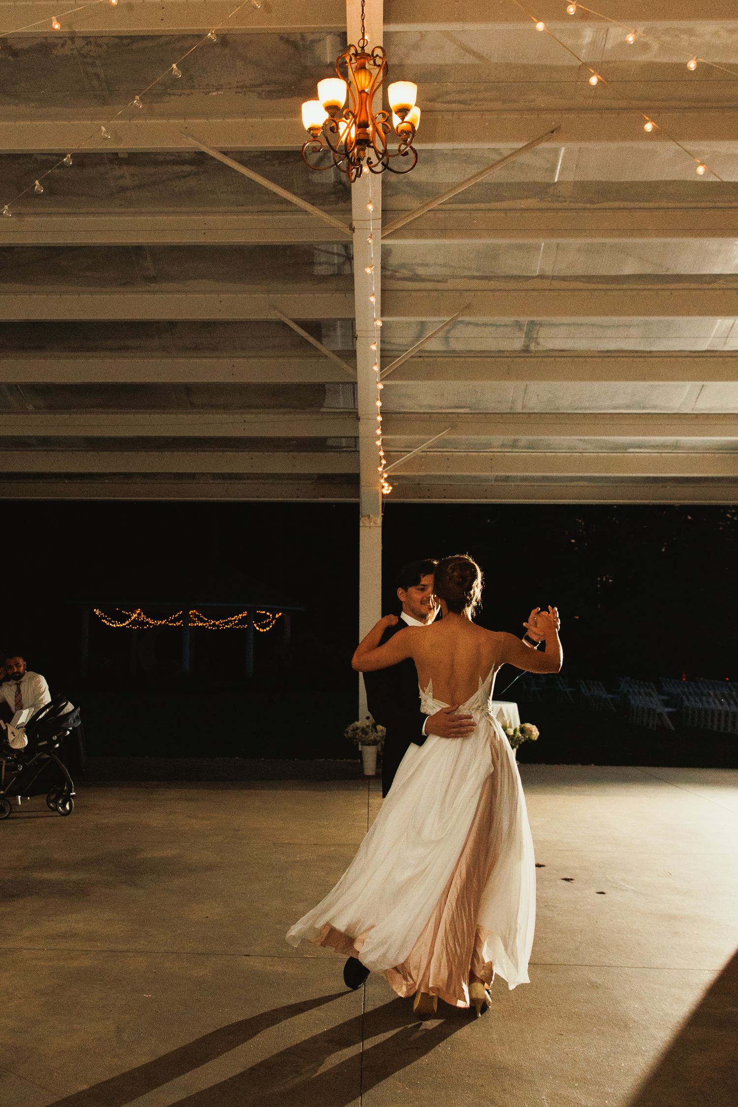 Couples dancing in an elegant reception hall with string lights and wooden beams.