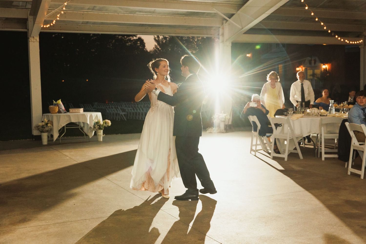 Wedding reception dance floor illuminated by warm spotlights and string lights.
