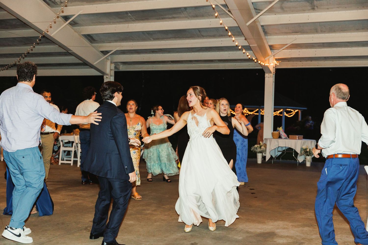 Large group of wedding guests dancing together on wooden dance floor.