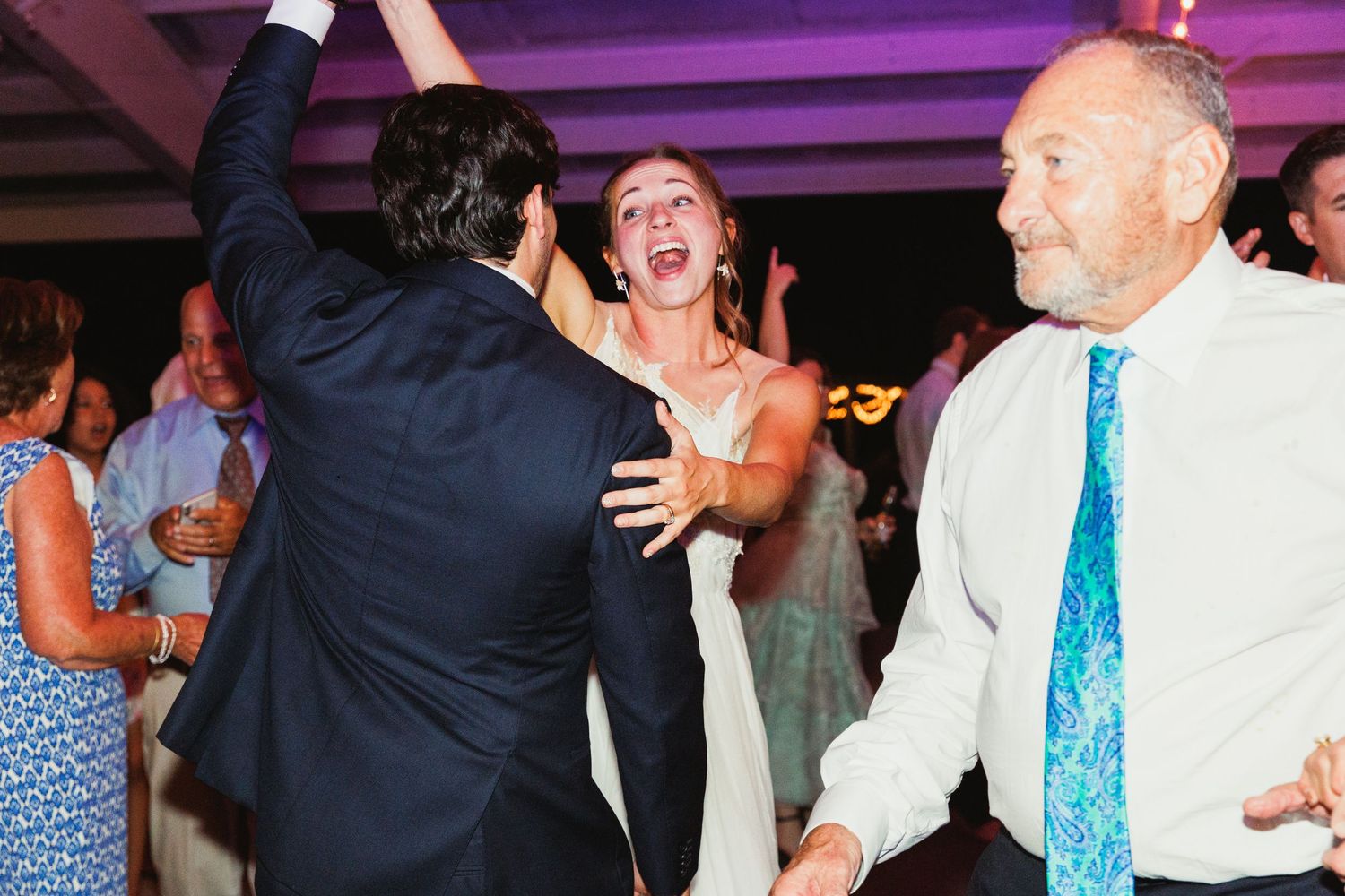 Wedding reception dance floor illuminated with purple lighting and string lights overhead.