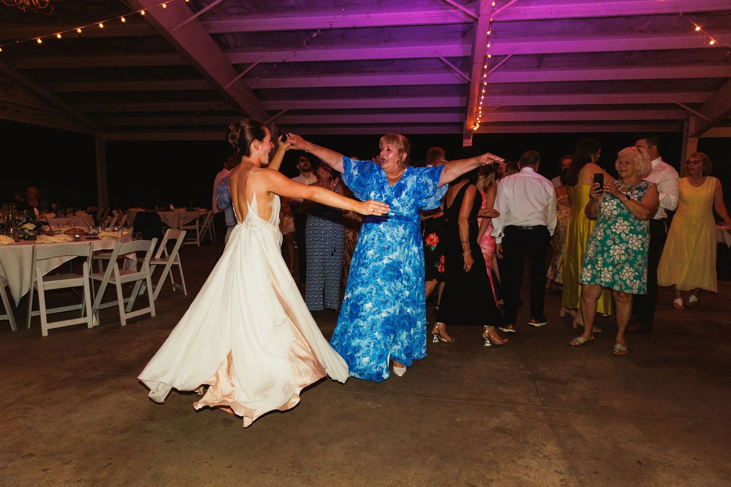 Guests dancing energetically under purple lighting at an outdoor wedding reception.