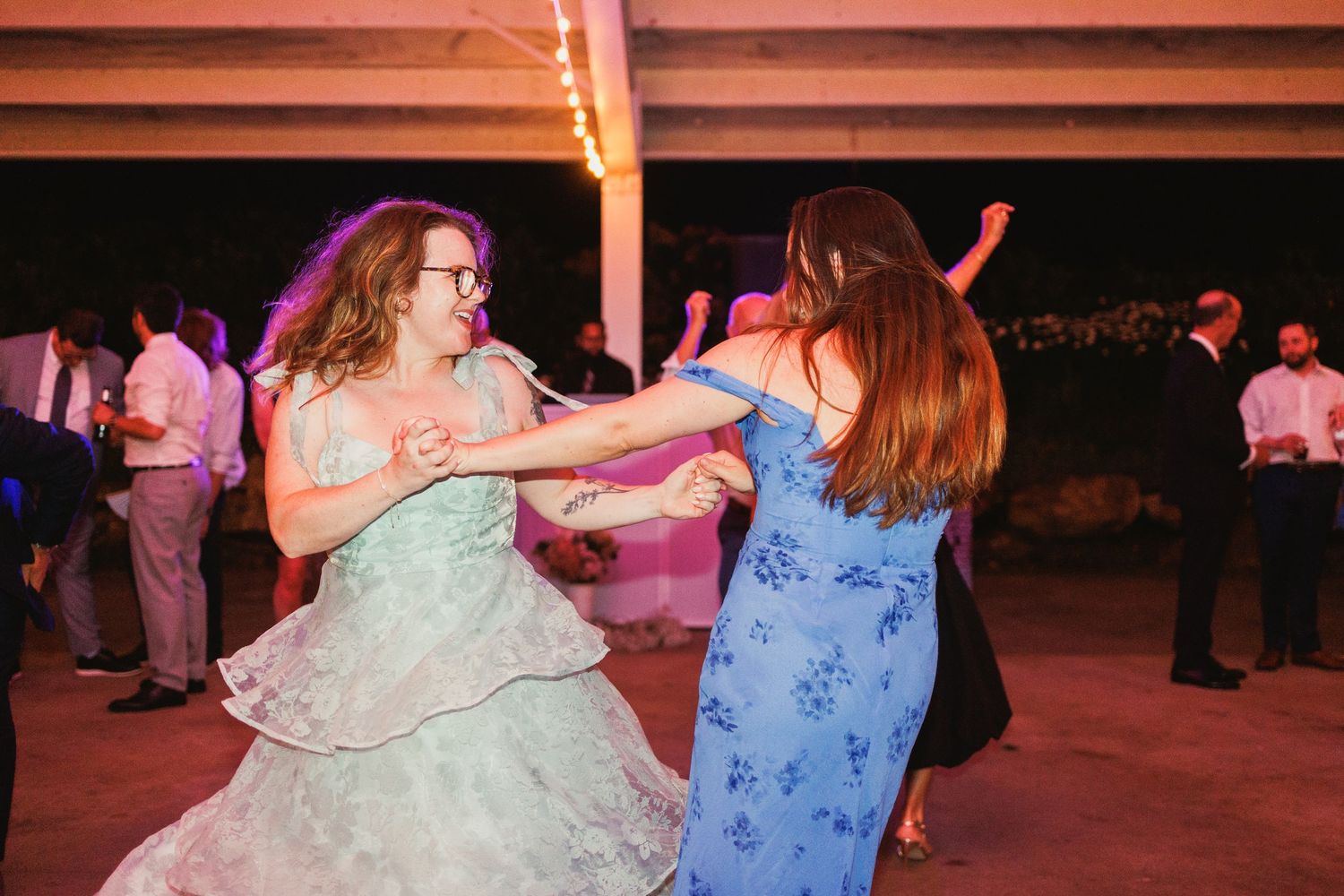 Wedding party members twirl and dance under colorful lighting at an evening celebration.