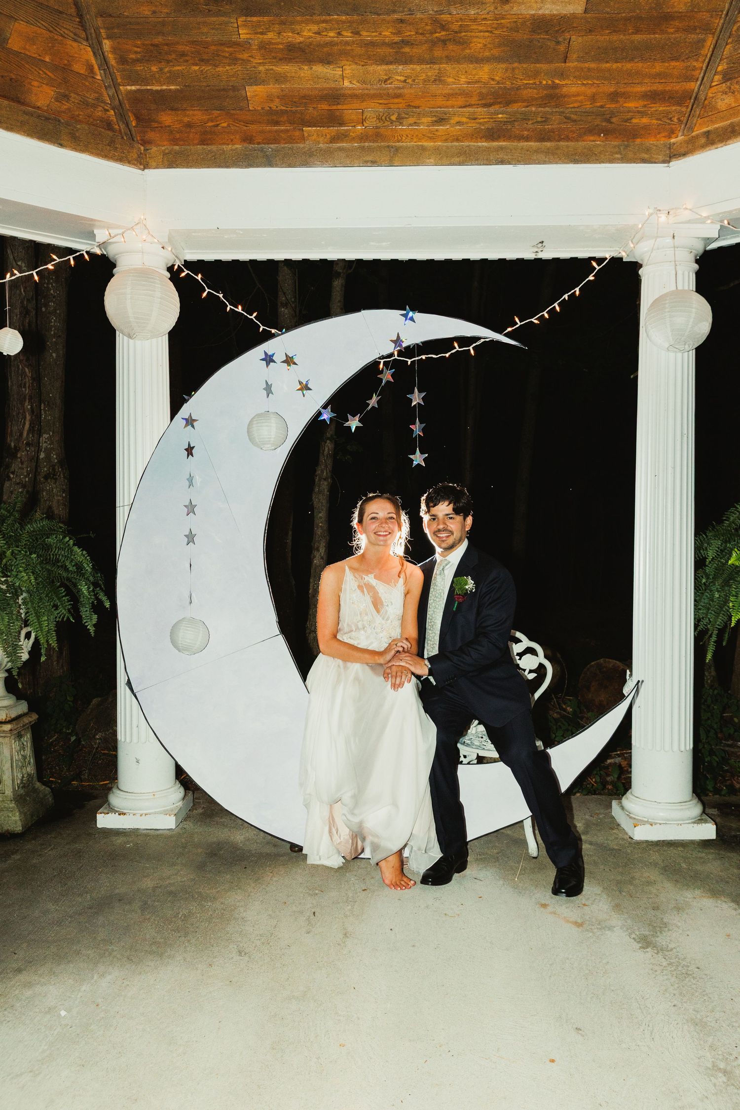 Wedding couple poses in front of decorative crescent moon backdrop with twinkling lights.