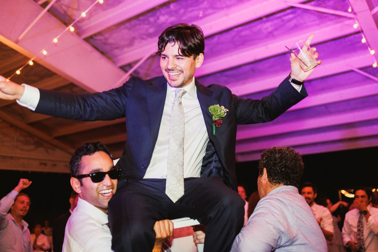 Dance floor filled with celebration under purple-lit ceiling at wedding reception.