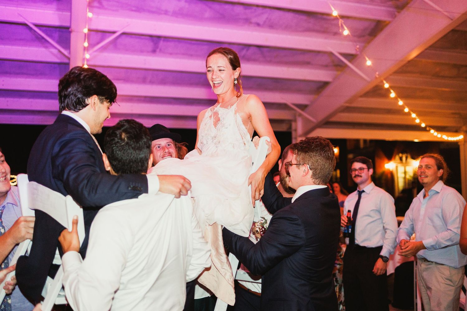 Energetic dancing and celebrations under purple lighting at wedding reception.