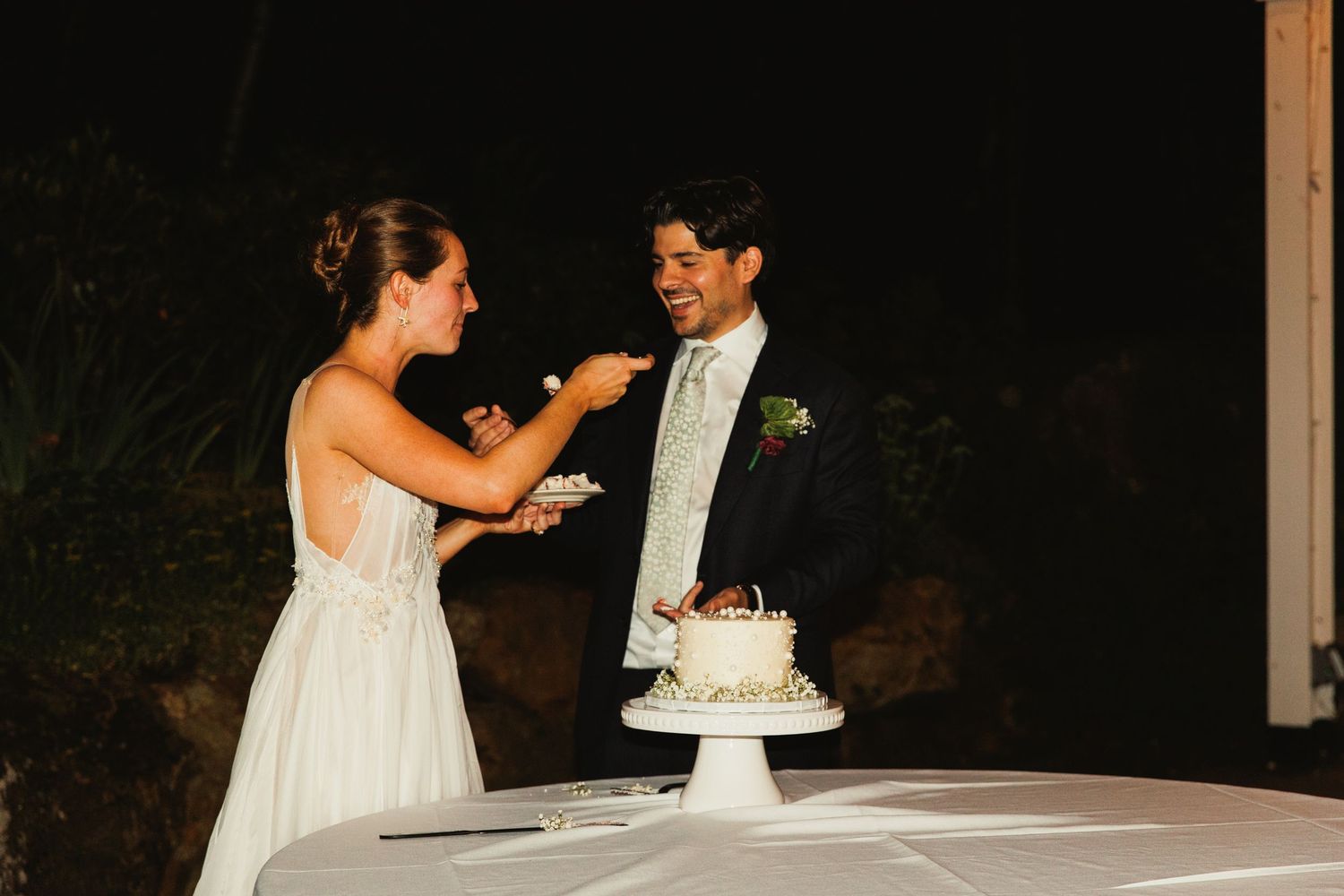 Couple sharing a joyful moment during their wedding cake cutting ceremony under warm lighting.