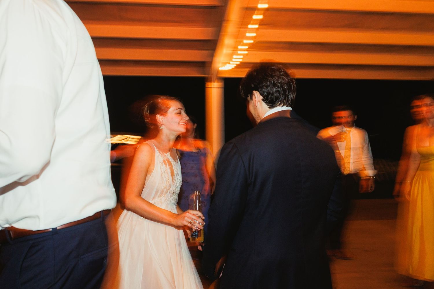 Wedding guests dancing and celebrating at an indoor reception with orange ambient lighting.