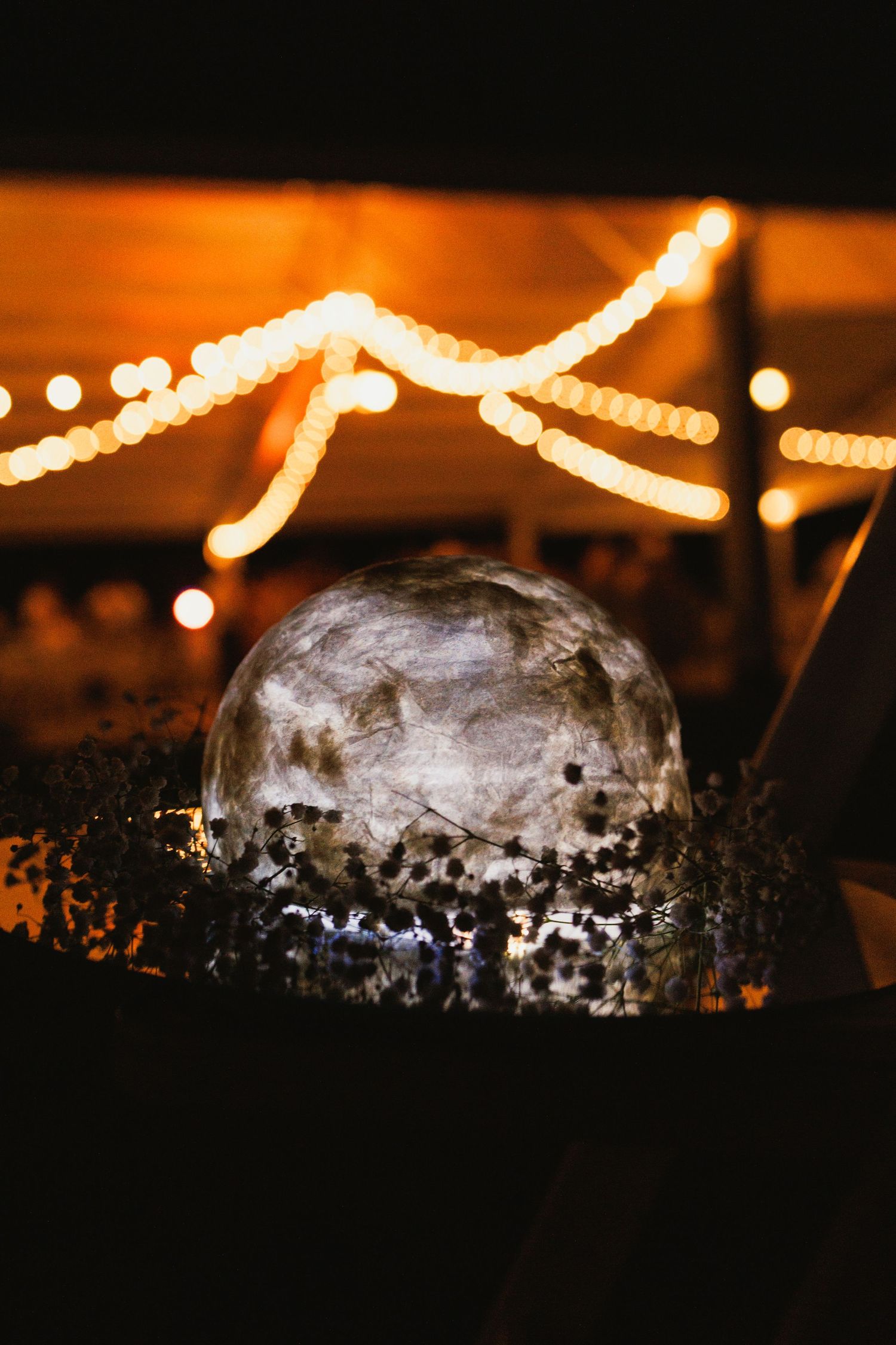 Wedding cake silhouette against dark background with string lights creating romantic ambiance.